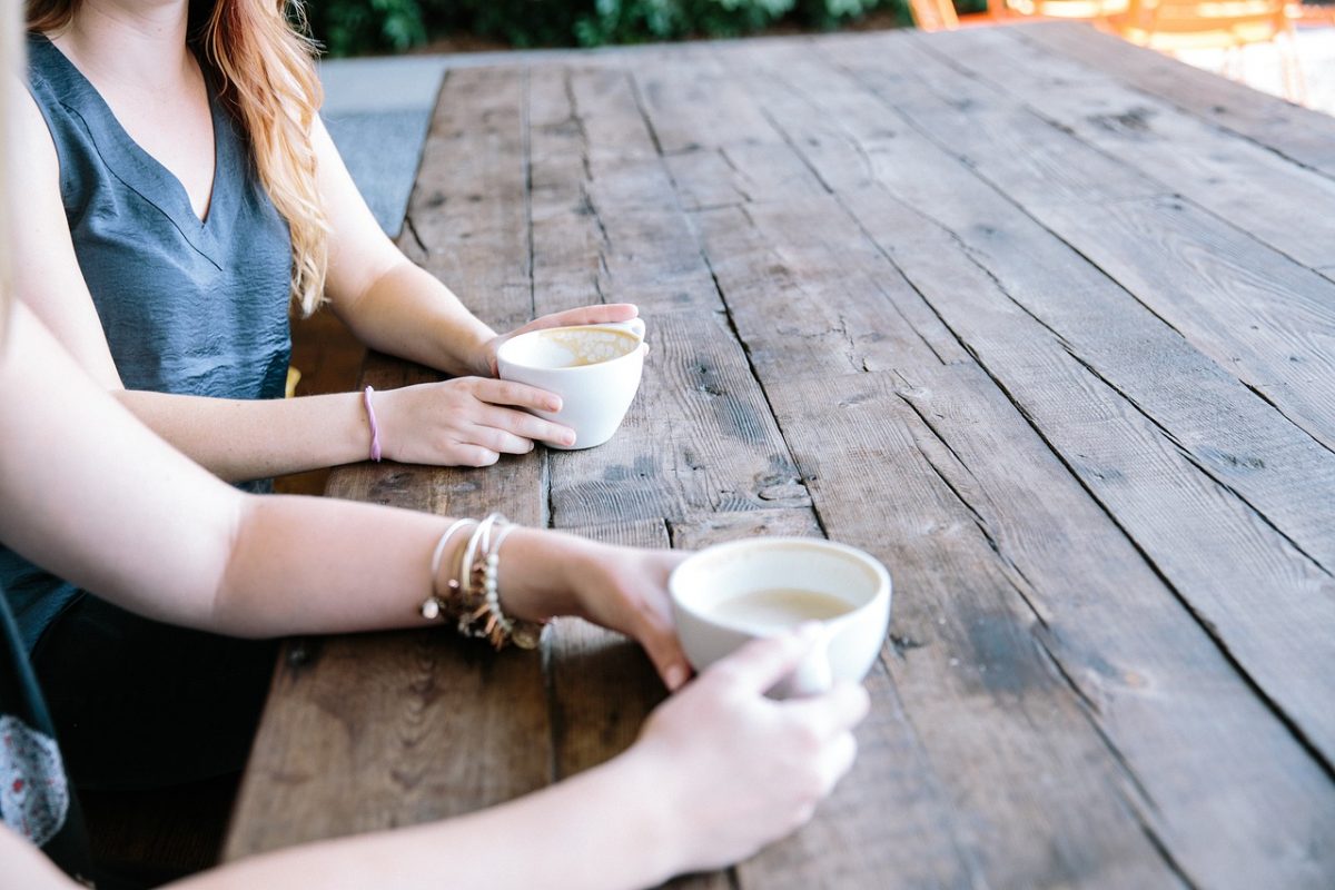Two people having a cuppa on a wooden table outdoors