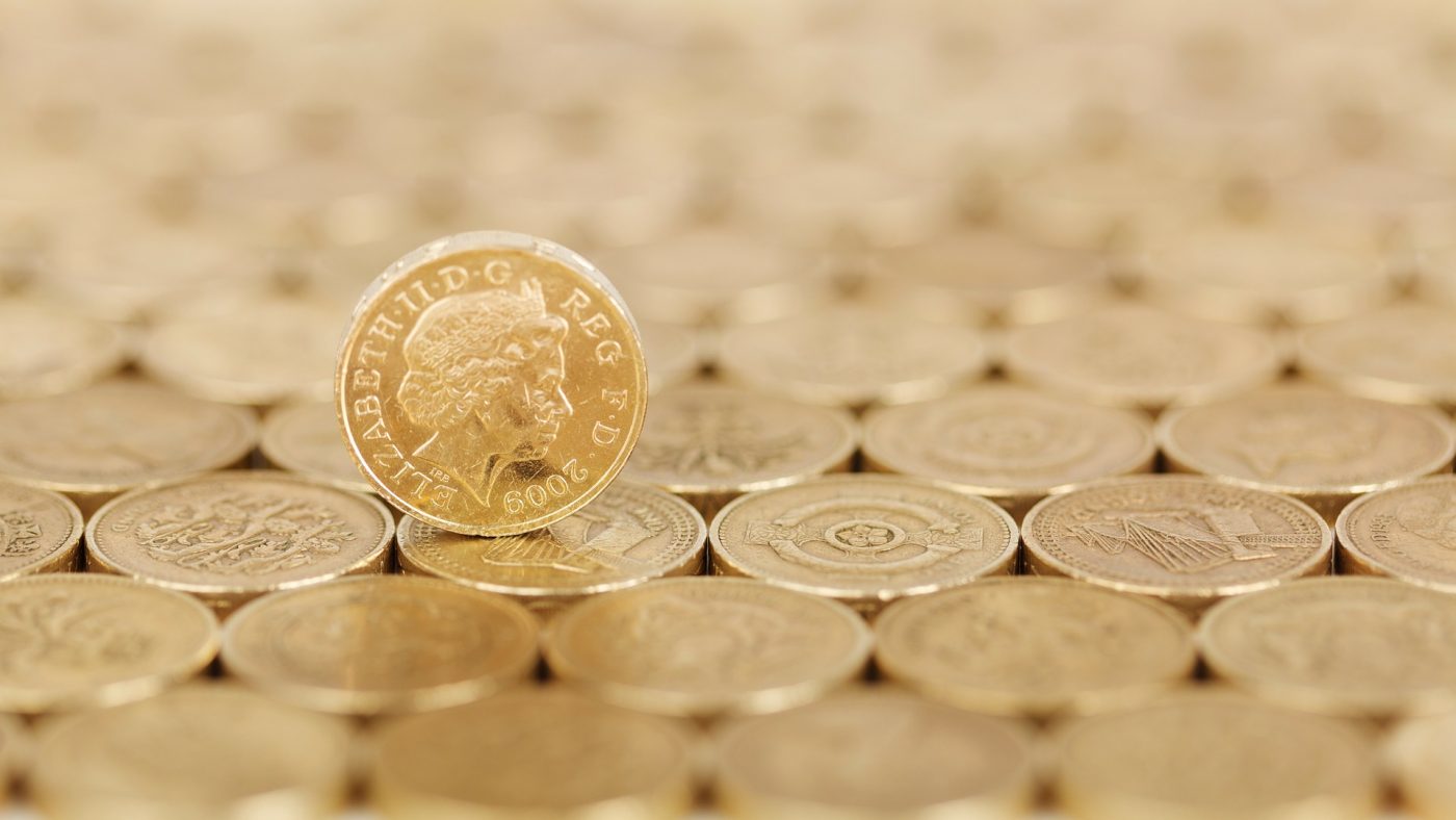 A perfectly flat surface of pound coins, with a single pound coin sitting atop them on its side