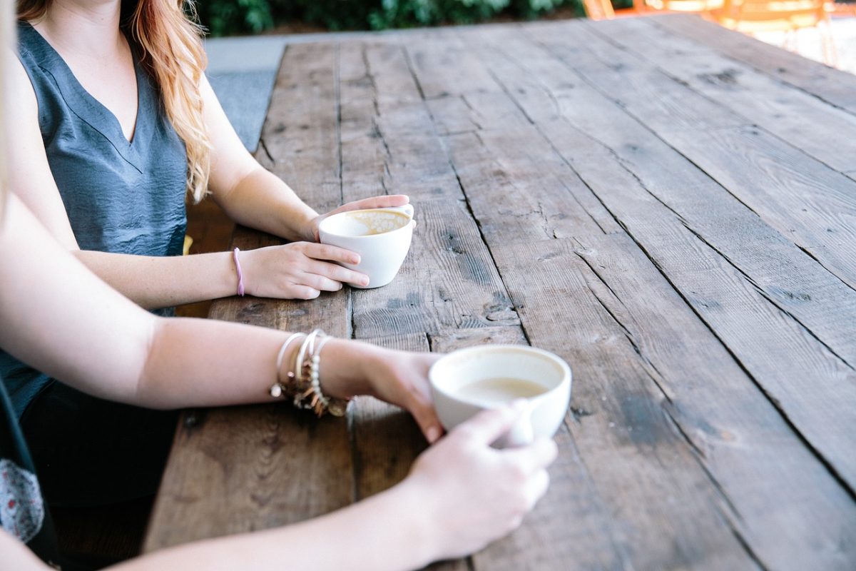 Two people sitting at a bench, each with a cup of hot drink