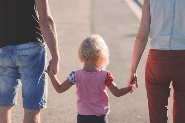 A child walking between their parents, holding both their hands